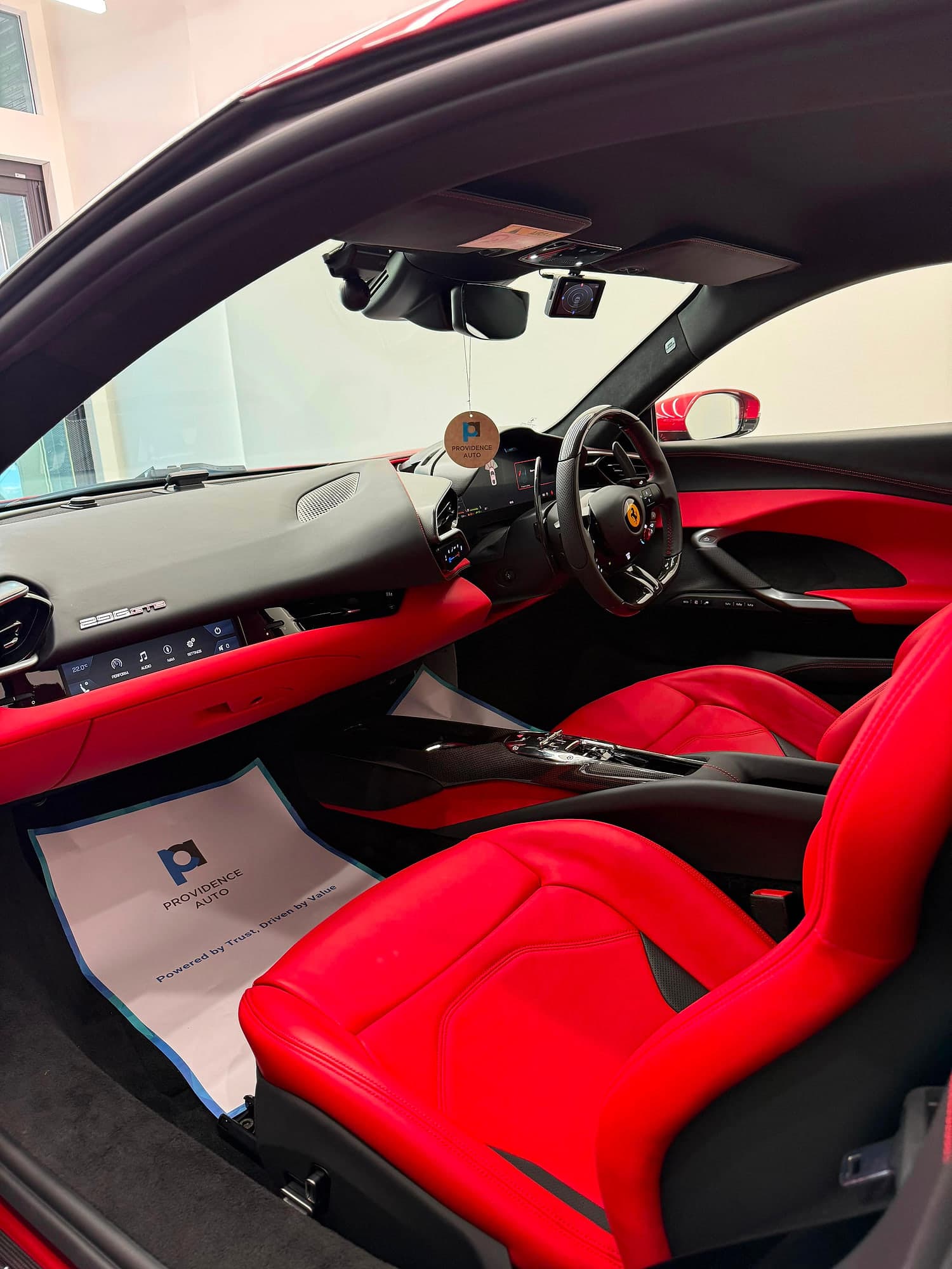 The red leather cabin of a right-hand-drive Ferrari 296 GTB with a Providence Auto mat laid in the footwell