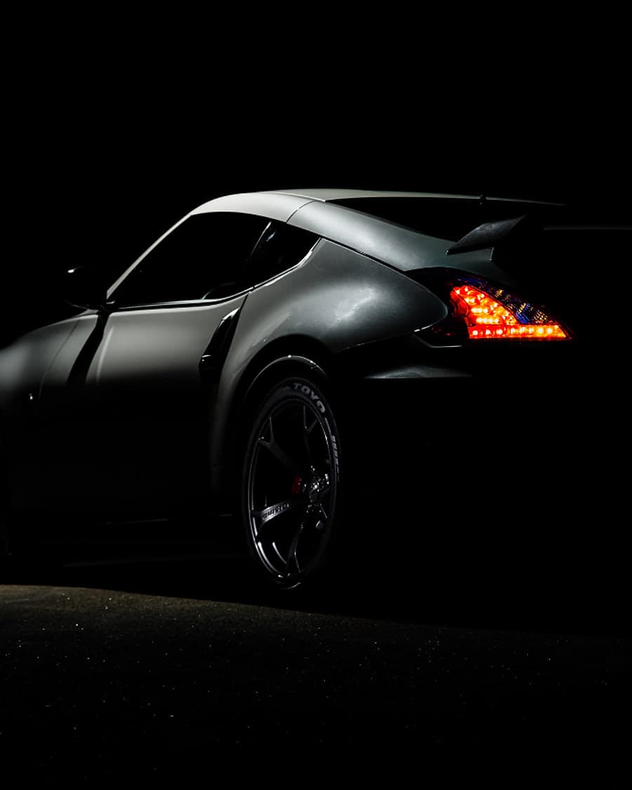The rear of a dark coupé at night with its tail lights lit